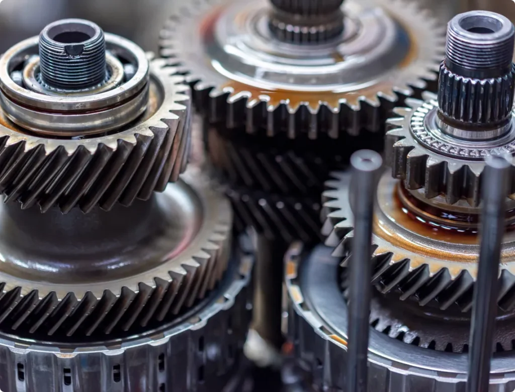 Allied Automotive: Close-up of interlocking metal gears with visible oil and intricate teeth, showcasing industrial machinery components. The gears are tightly arranged, highlighting their mechanical details and precision engineering.