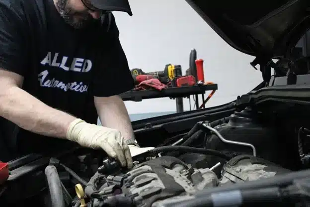 Technician at Allied Automotive working under the hood of a vehicle, performing engine diagnostics and repairs.