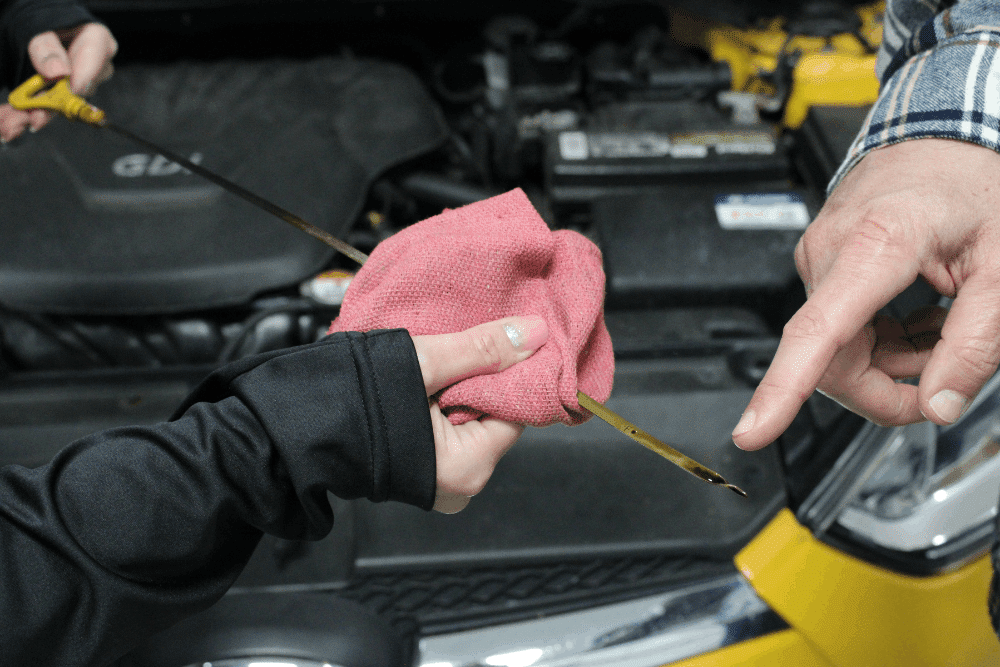 Oil change services in Allentown, PA by Allied Automotive. Image of a technician checking engine oil with a dipstick and cloth under the hood, emphasizing proper oil levels, engine protection, and preventative maintenance.