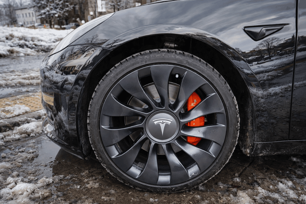 Tesla brake issues, Tesla repair in Allentown, PA by Allied Automotive. Image of a Tesla wheel with performance brake caliper on a snowy road, highlighting professional electric vehicle brake inspections, rotor service, and winter-ready braking performance.