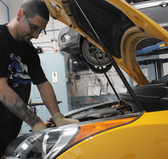 Auto mechanic working under the hood of a yellow vehicle at Allied Automotive in Allentown, PA, performing diagnostics or summer car maintenance service in a professional repair bay.