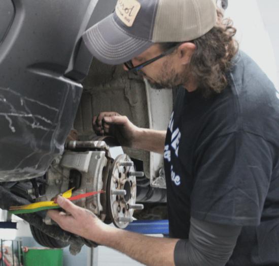 Comprehensive Road Trip Brake Repair and A/C Service in Allentown, PA At Allied Automotive. A mechanic inspecting a car's disc brake assembly and using a thickness gauge to measure the brake pad wear during a brake service.